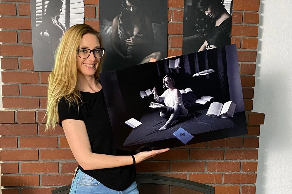 A smiling client holding a large canvas print of her boudoir portrait against a brick wall