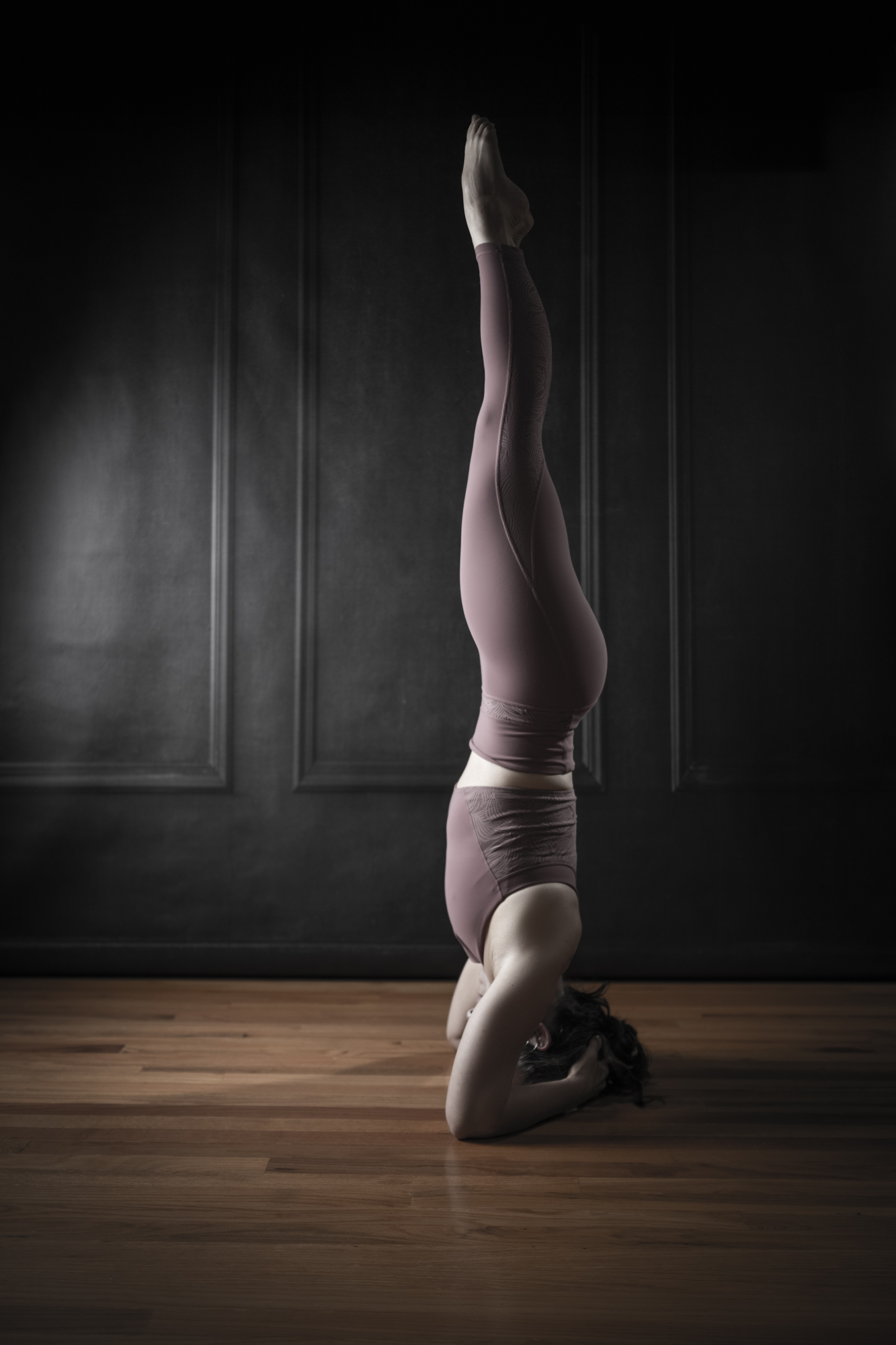 Portrait of a woman in a headstand against a dark wall