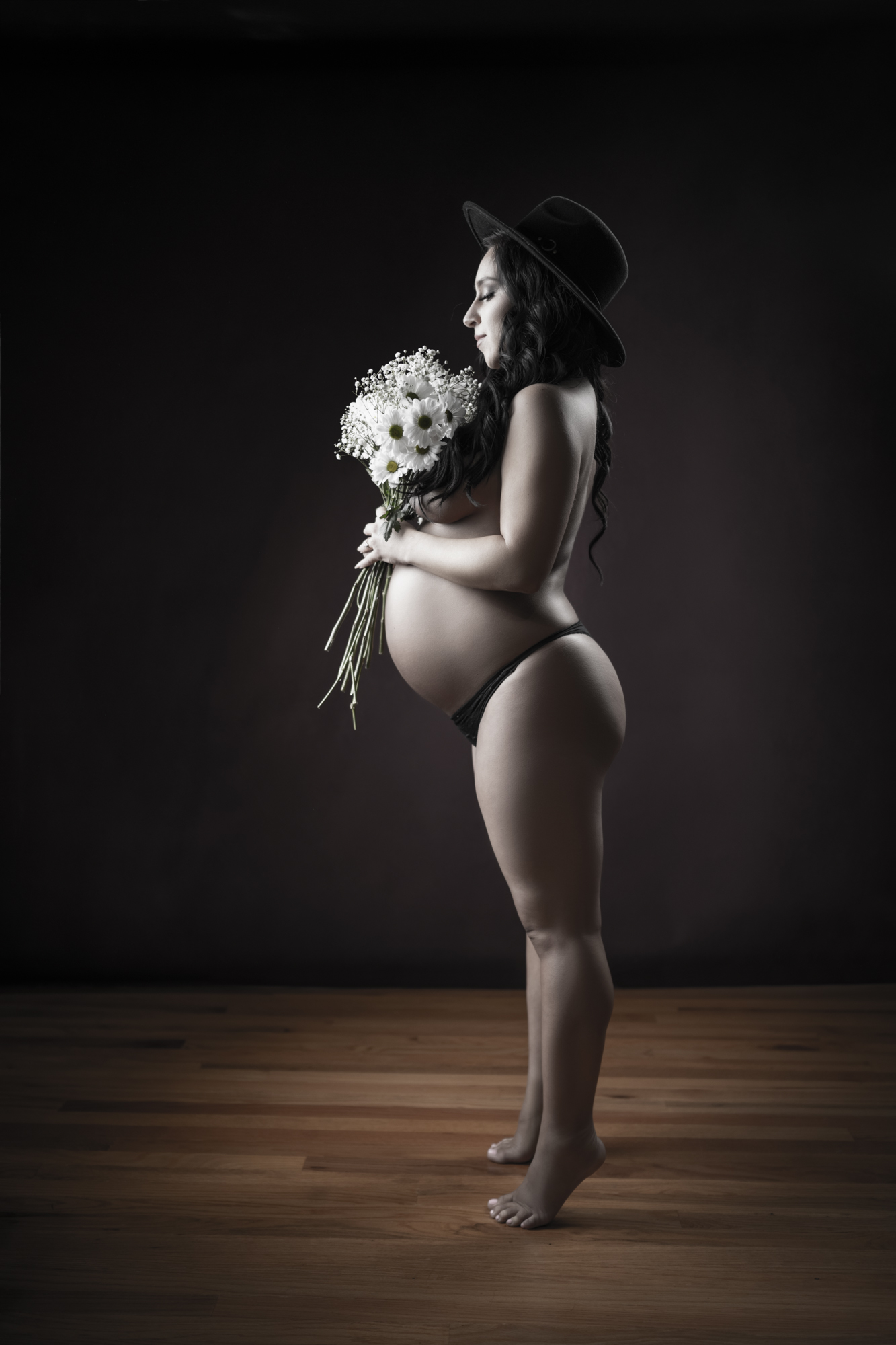 Profile portrait of a pregnant woman in a black hat holding a white bouquet